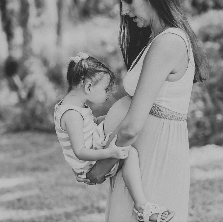 Little girl kisses her mother's growing baby bump in anticipation of her new sibling in Fort Myers, Florida.