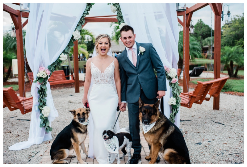 Bride, groom and 3 dogs stand at altar smiling on wedding day.
