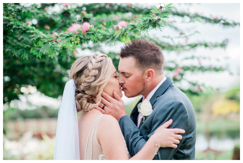 Bride and groom share a kiss under a garden tree on wedding day