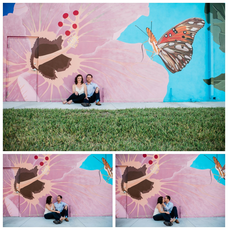Engaged couple smiles in front of painted hibiscus wall in Downtown Fort Myers.