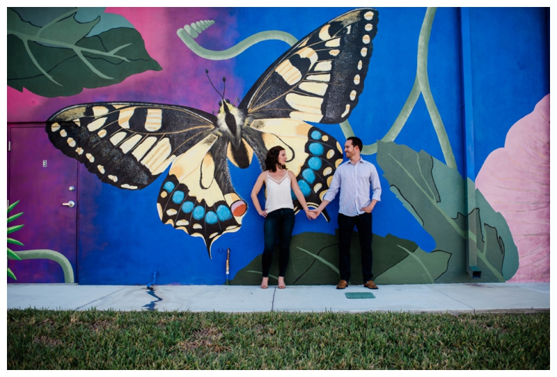 Bride and groom to be hold hands in front of butterfly mural in Fort Myers, Florida.