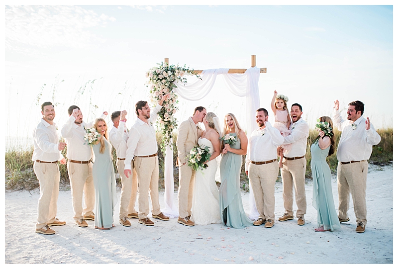 Bridal party in light sage green, ivory and beige celebrate newlyweds on the beach at Pink Shell Beach Resort & Marina