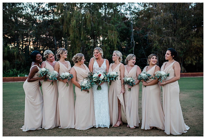 Bride stands with 8 bridesmaids dressed in light tan bridesmaids gowns in Naples, Florida.