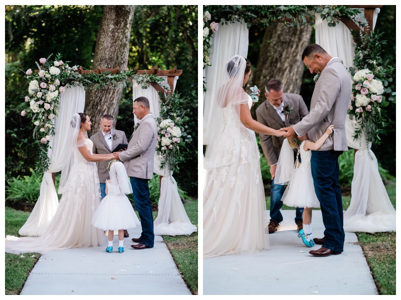 Bride and groom stand at draped arch during Southwest Florida wedding ceremony with their daughter the flower girl