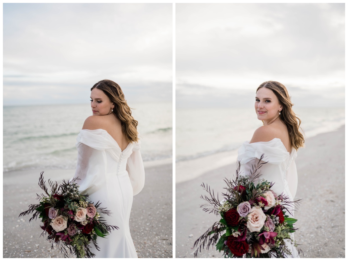 winter Florida bride stands seaside in long sleeve off the shoulder bridal gown and dark toned bridal bouquet 