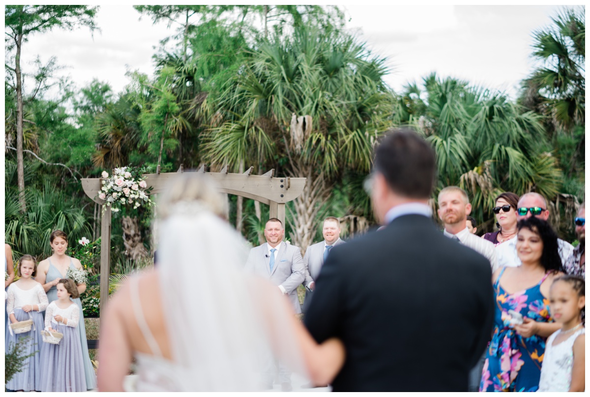 bride walks down the aisle as groom smiles during South Florida outdoor garden wedding ceremony