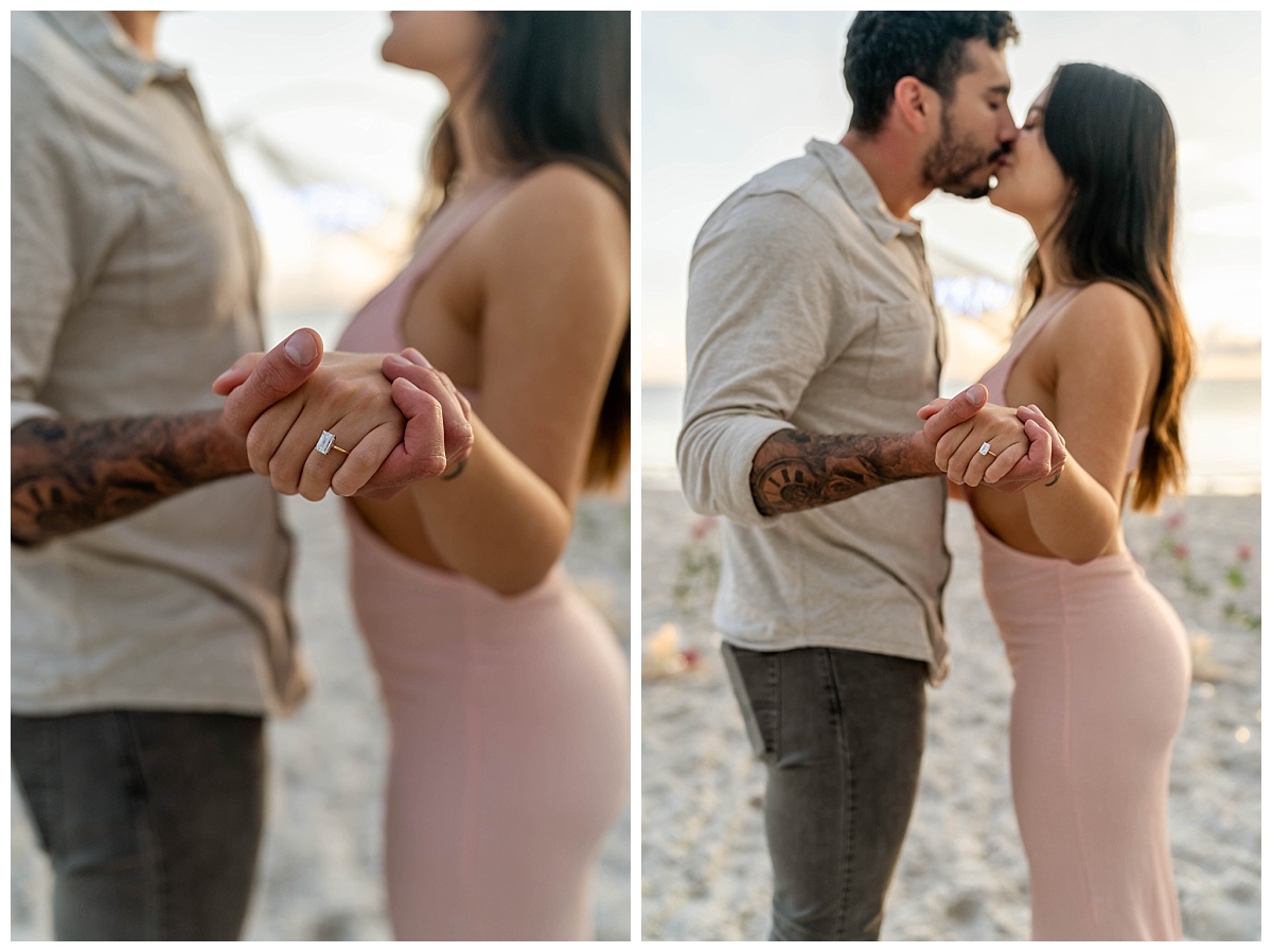 couple holds hands on florida beach after proposal. woman wears emerald cut engagement ring
