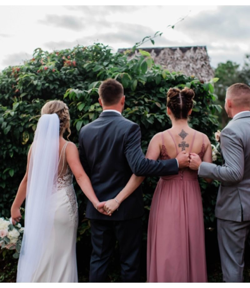 Maid of honor and bride hold hands as best man and groom fist bump on wedding day.